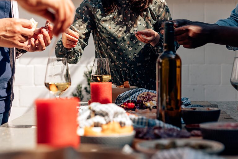 point of view of the table at a party with candles and wine, tapas, salami, fruit. hands picking up food.